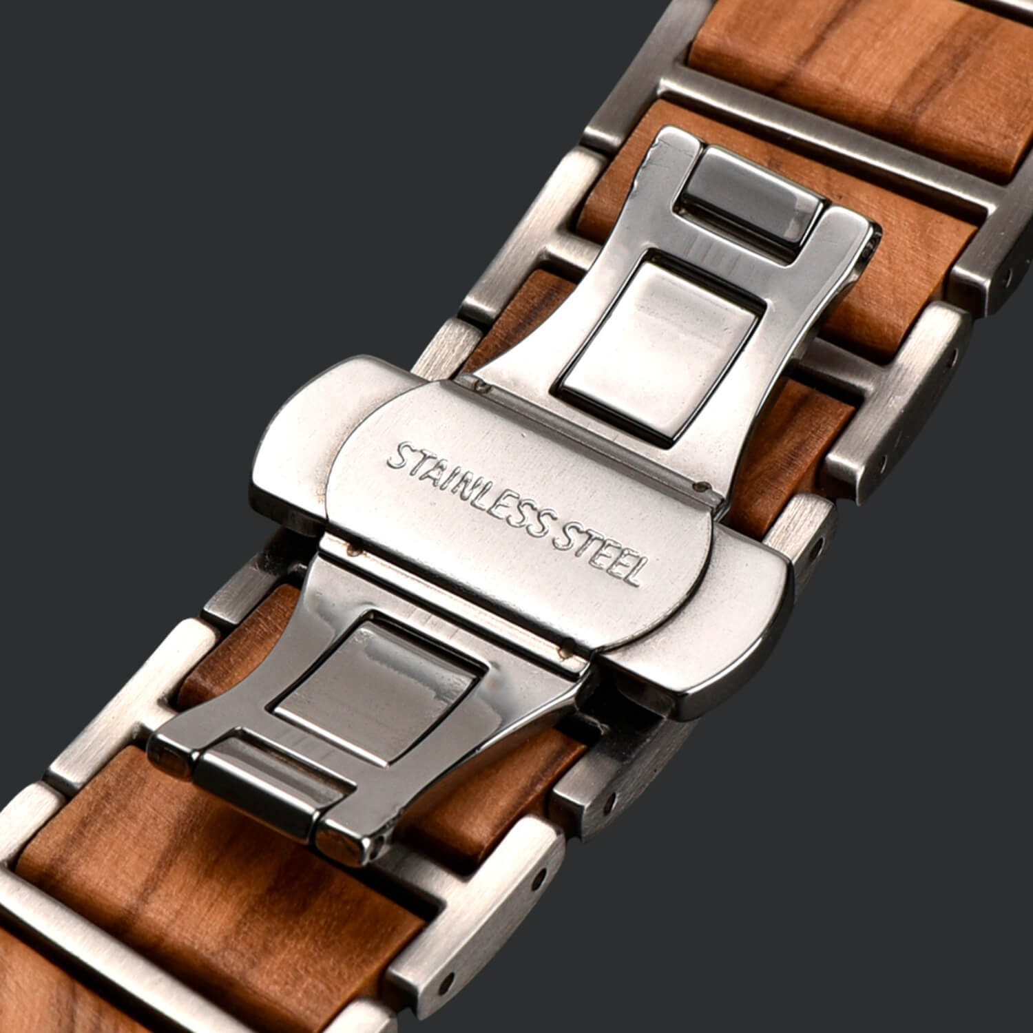 Close-up of an apple watch strap with wooden finish and metal butterfly clasp on a dark background