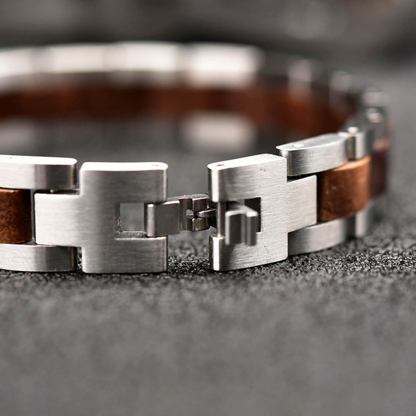 Close-up of a silver bracelet with walnut wood accents on a textured surface.