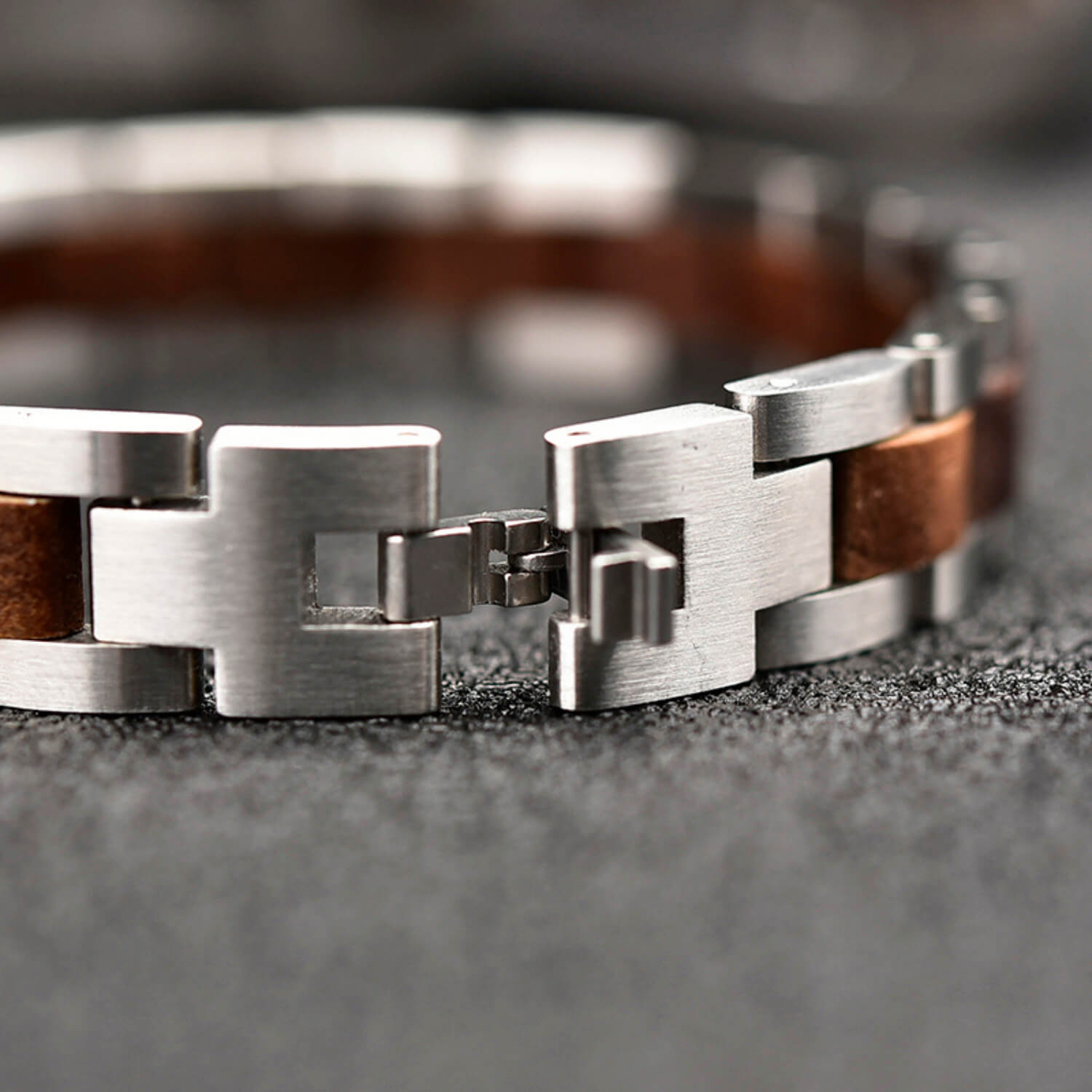 Close-up of a silver bracelet with walnut wood accents on a textured surface.