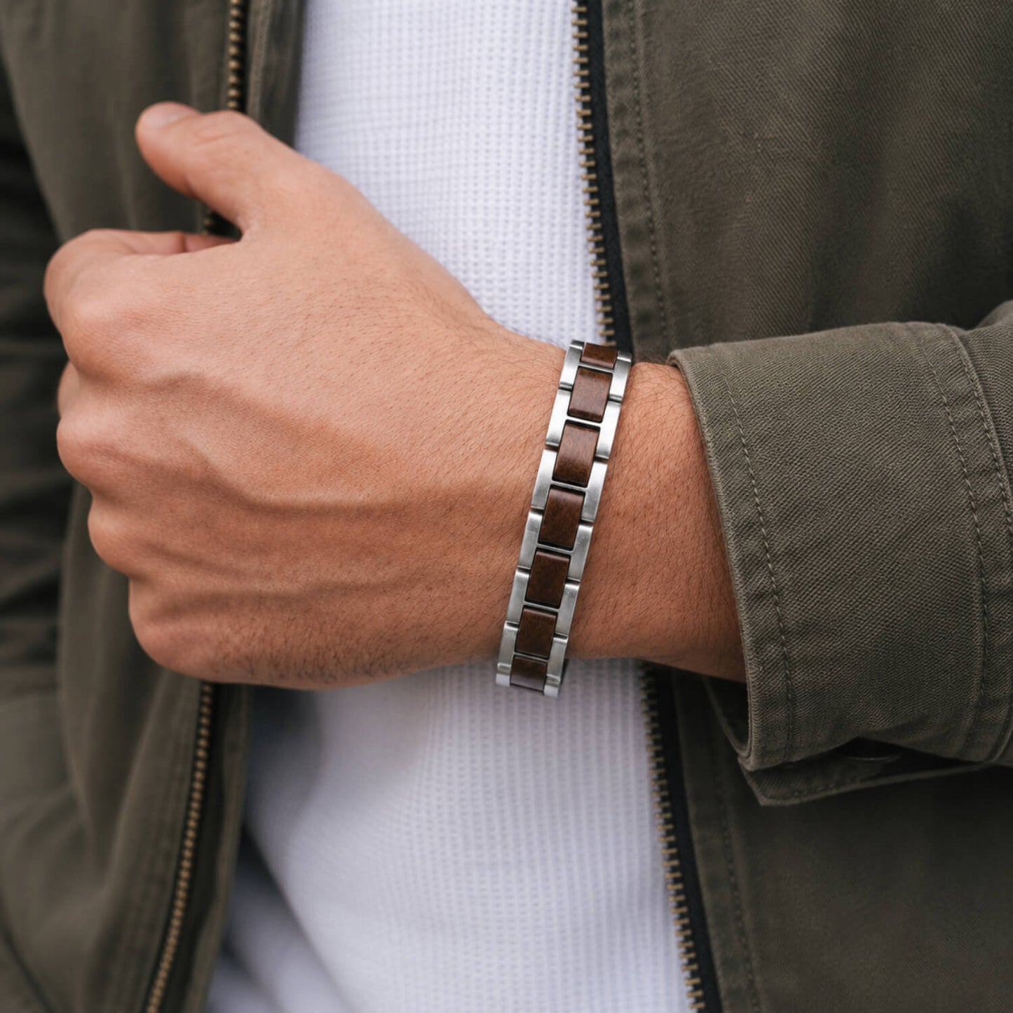 Person wearing a steel and wood bracelet on a wrist with a green jacket and white shirt.