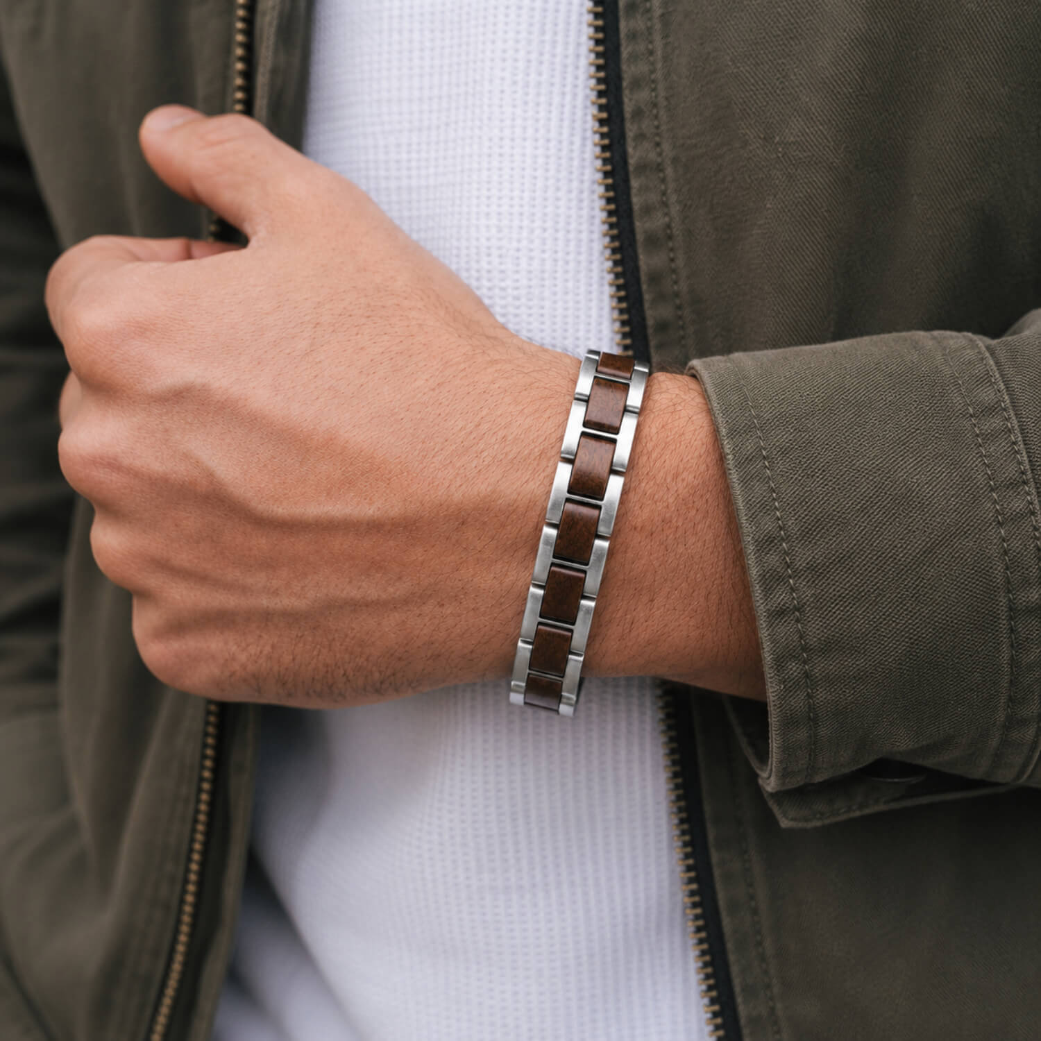 Person wearing a steel and wood bracelet on a wrist with a green jacket and white shirt.